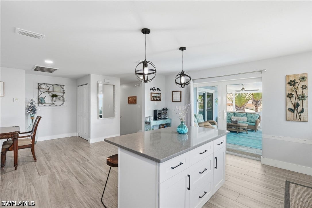 Kitchen island featuring a light-colored countertop, white cabinetry with dark hardware, and two pendant light fixtures - Virtually Edited Image