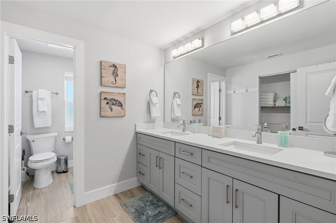 Dual vanity with gray shaker cabinetry, integrated sinks, and light-toned countertops - Virtually Edited Image