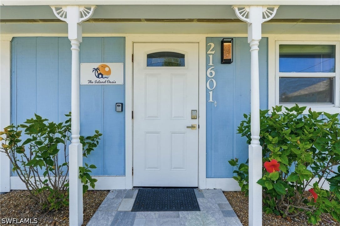 Entryway featuring a paneled door with an arched window, light blue siding, and white architectural columns - Virtually Edited Image
