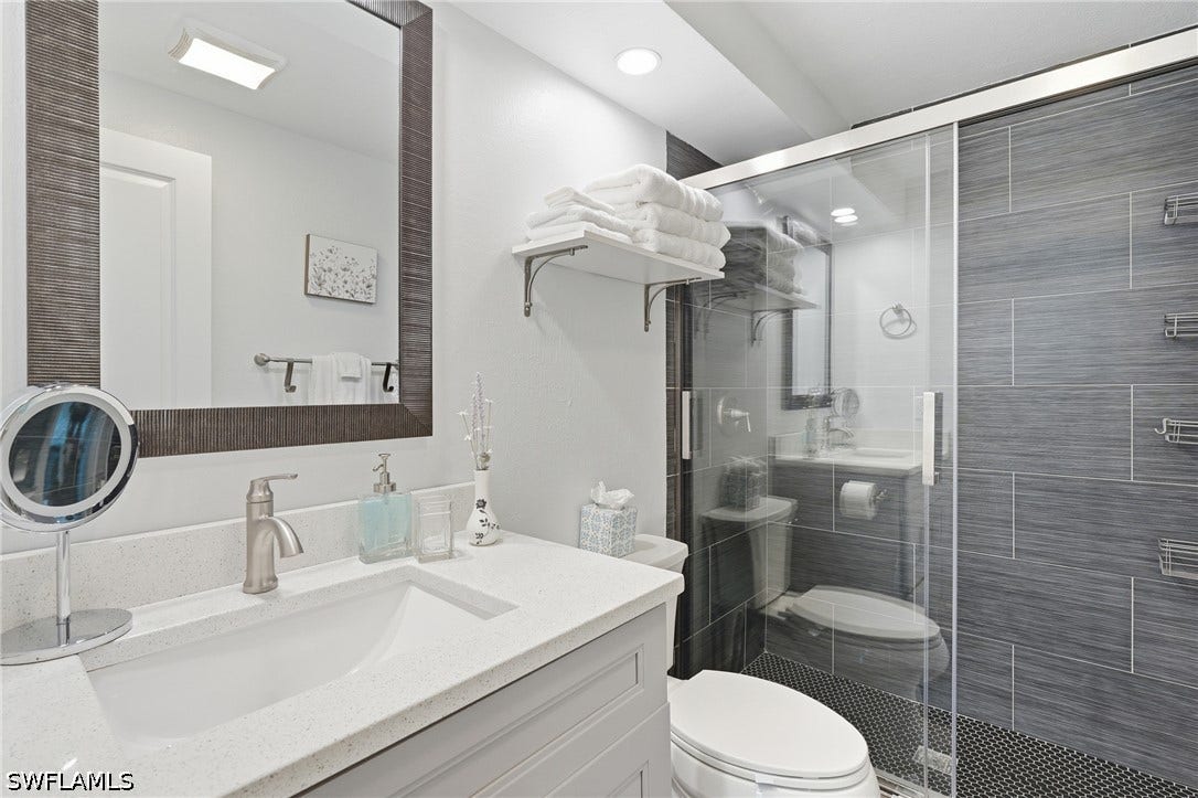 Bathroom featuring a frameless glass shower enclosure with gray horizontally tiled walls and a dark mosaic tile floor - Virtually Edited Image