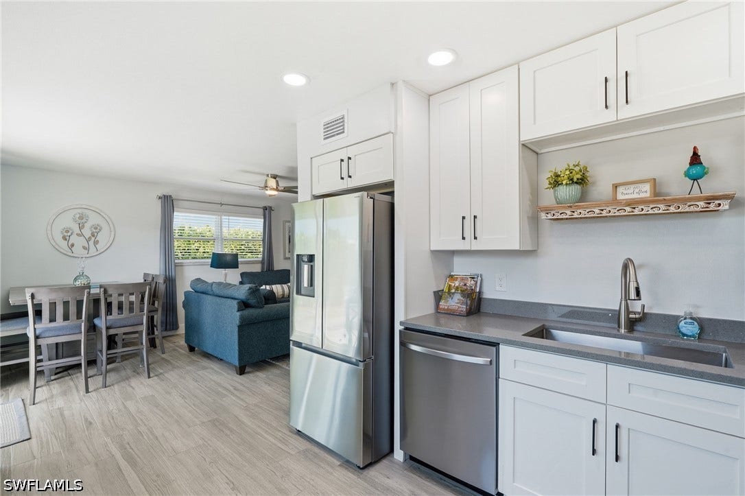Open concept living area featuring contemporary white cabinetry, stainless steel appliances, stone countertops, and wood-finish flooring - Virtually Edited Image