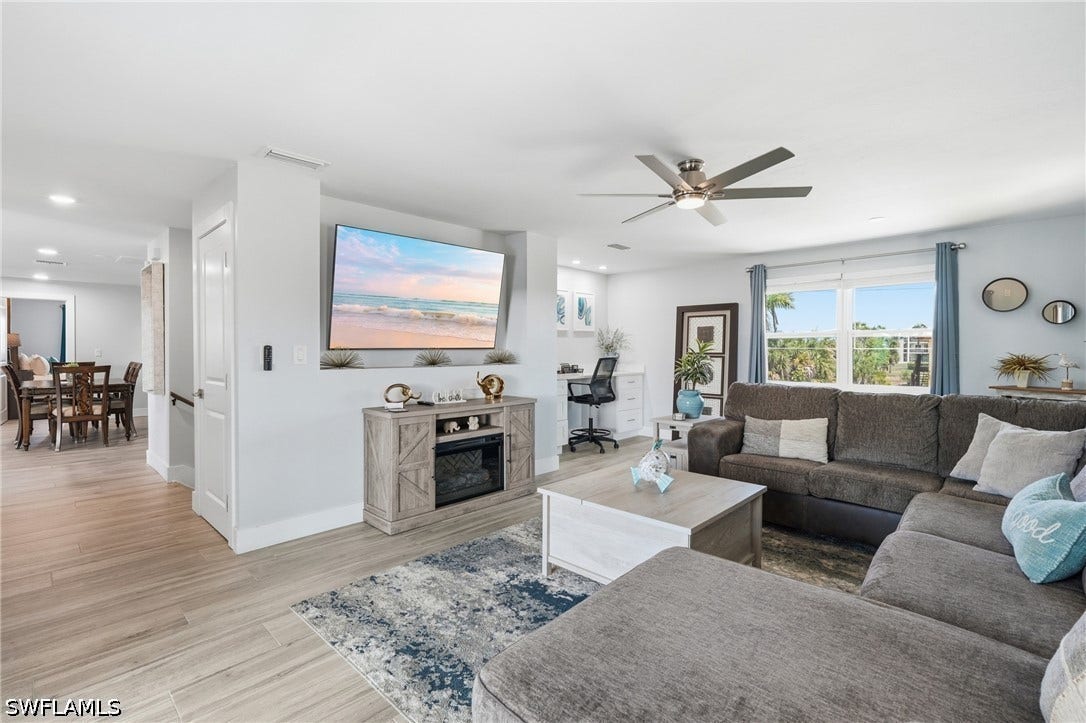 Open concept living area featuring wood-finish flooring, recessed lighting, a modern ceiling fan, large windows, and a built-in media console - Virtually Edited Image