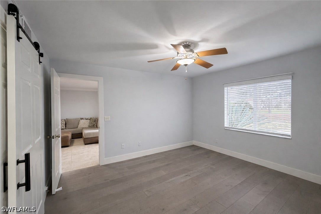 Unfurnished bedroom featuring a barn door, light wood-style floors, and ceiling fan
