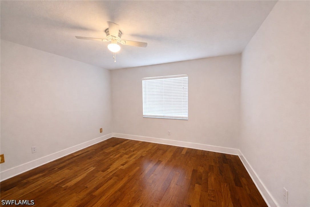 Empty room featuring dark wood-type flooring and a ceiling fan