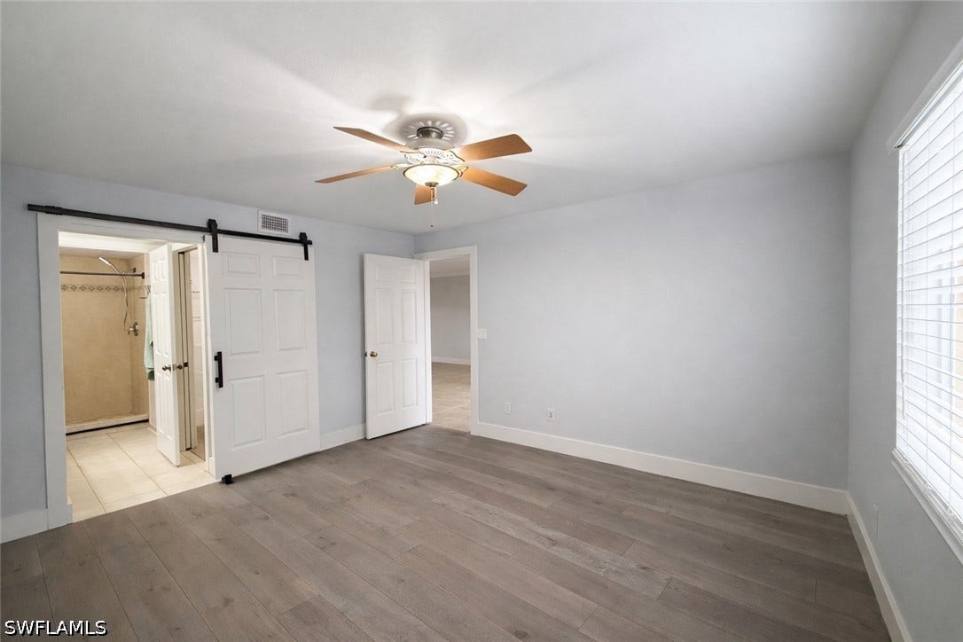 Unfurnished bedroom featuring a barn door, hardwood / wood-style floors, a ceiling fan, and multiple windows