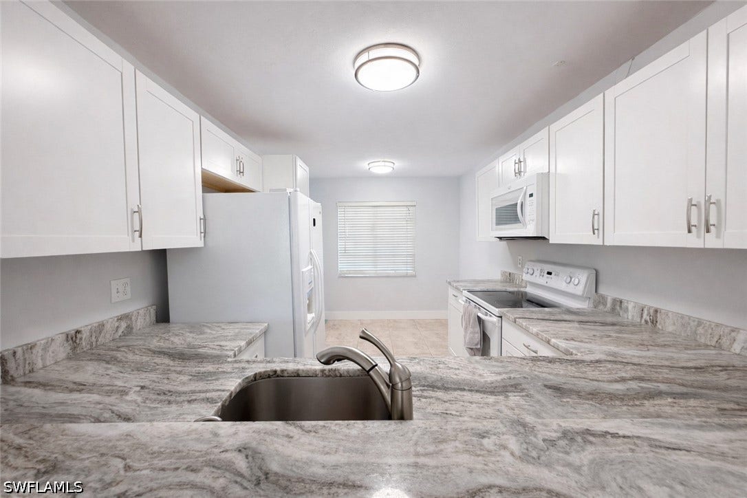 Kitchen featuring white cabinetry, white appliances, and light stone counters