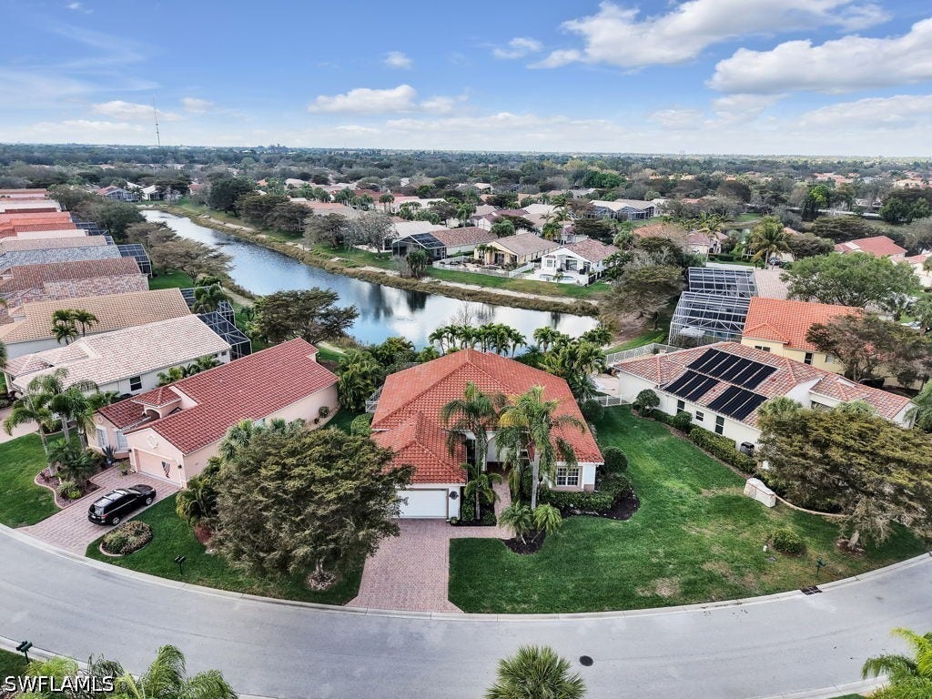 Single-story residence featuring a red tile roof, lush green landscaping, and a paver driveway