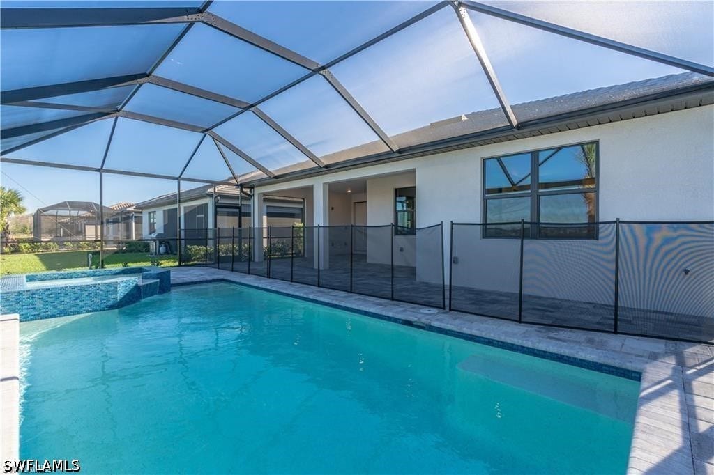Screened outdoor living space featuring a swimming pool, integrated spa, and a pool safety fence
