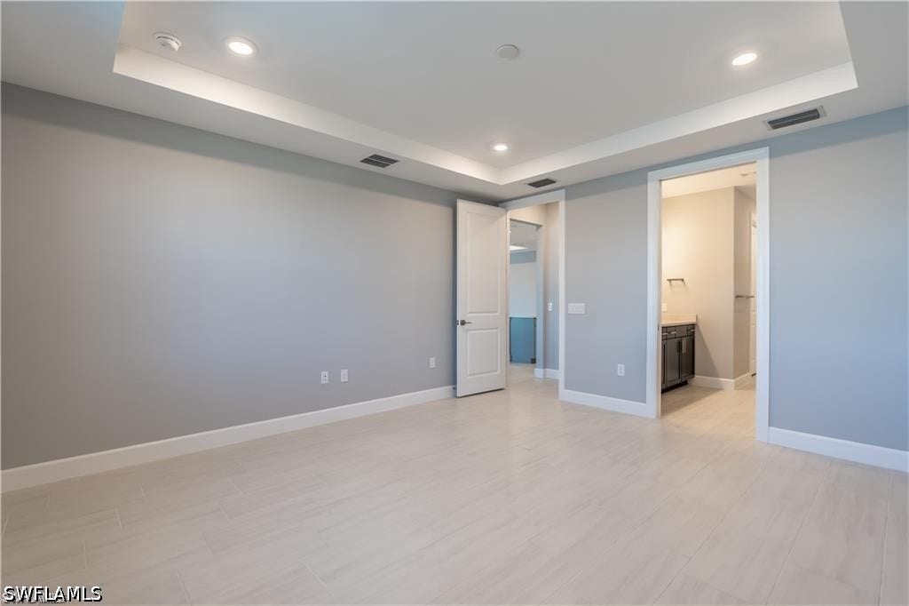 Recessed lighting, tray ceiling, light-toned wood-finish flooring, and white trim
