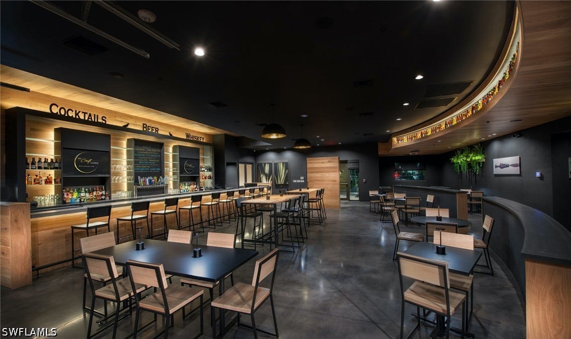 Polished concrete flooring, built-in bar with under-cabinet lighting, wood-finish wall panels, overhead recessed lighting, and a curved architectural wall detail