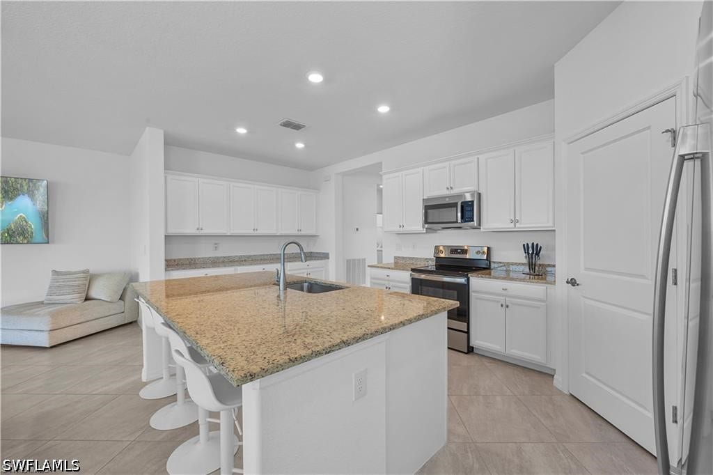 Kitchen featuring a large island with a sink, white cabinetry, recessed lighting, and stainless steel appliances including a range and microwave
