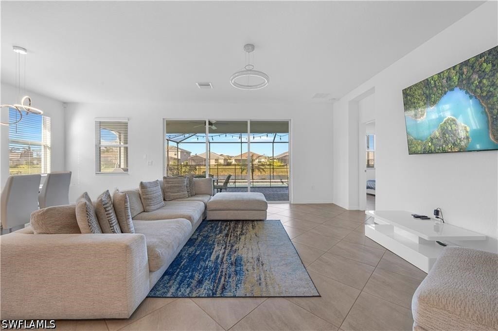 Expansive open-concept living area featuring diagonal tile flooring, a contemporary ceiling light fixture, and large sliding glass doors leading to a screened lanai