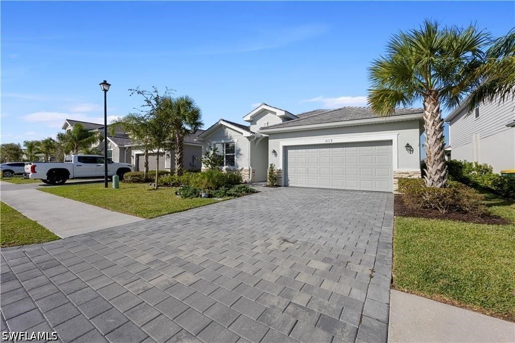 Paver driveway, attached garage, well-maintained landscaping with mature palm trees, and a concrete walkway