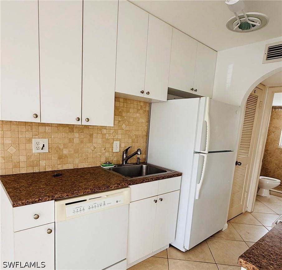 White cabinetry, mosaic tile backsplash, integrated dishwasher, double basin sink, and archway with louvered door