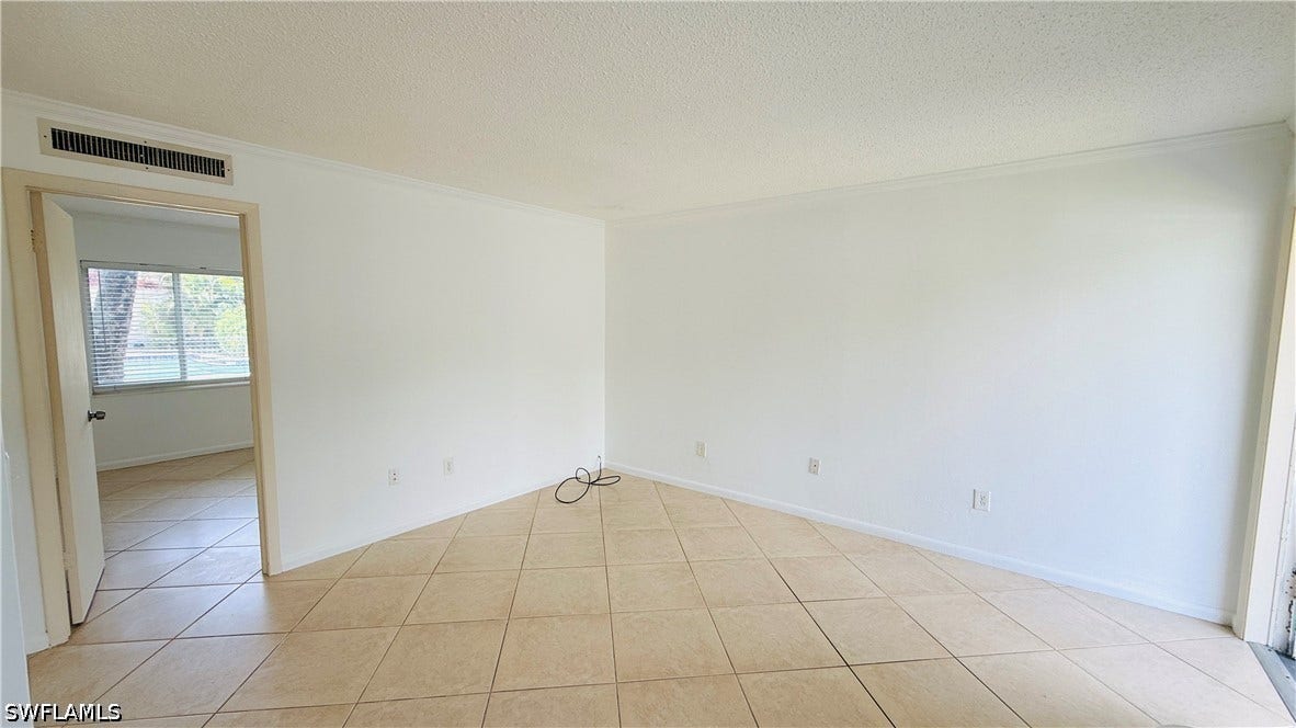 Light-colored diagonal tile flooring, white painted walls, crown molding, and a visible doorway leading to another room with a window