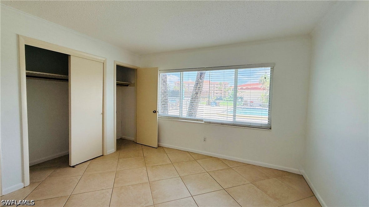 Tile flooring, two closet spaces with sliding doors, a window with blinds, and white painted walls
