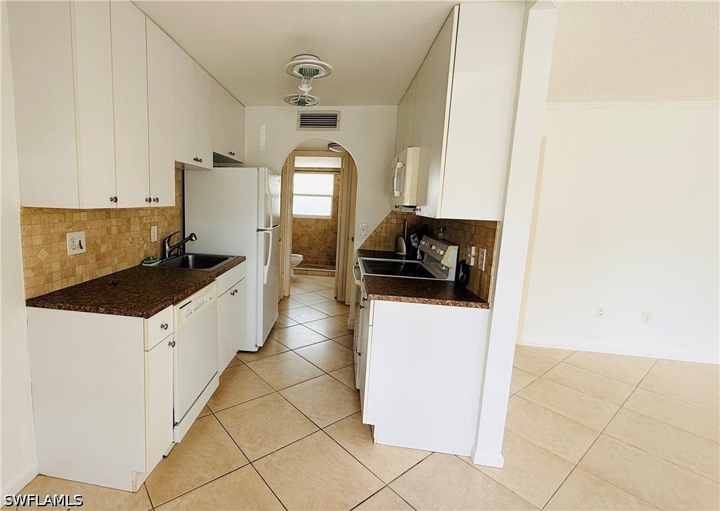 Kitchen featuring white cabinetry, dark speckled countertops, a tile backsplash, and tile flooring