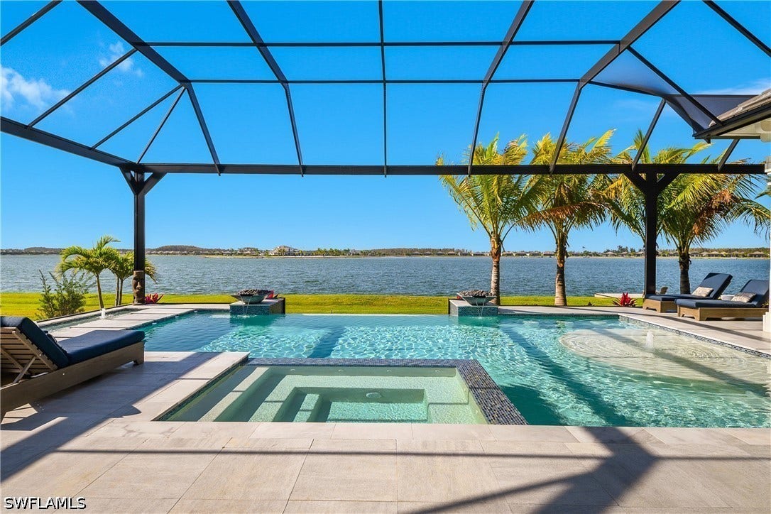 Sparkling inground pool overlooking WildBlue lake features a spillover spa, sun shelf, "lilly pad" bubblers, in pool bar with bar stools, infinity edge, fire/water fountain bowls, auto water filler, and surrounding travertine pavers