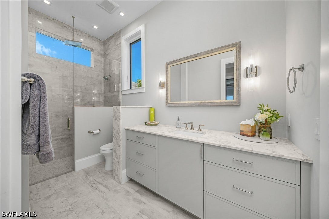 Guest ensuite bath with walk-in frameless shower and windows providing natural light.