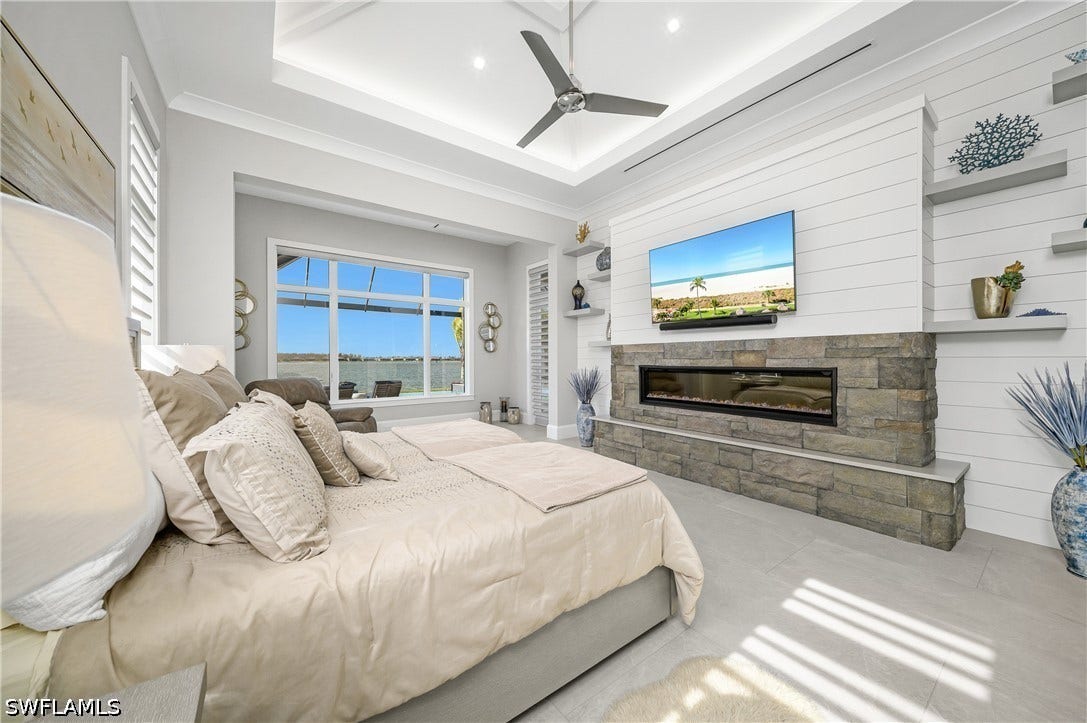Primary suite with private lanai entry, remote Hunter Douglas window coverings, custom built-in stone fireplace with floating shelves, lighted 15' tray ceiling.