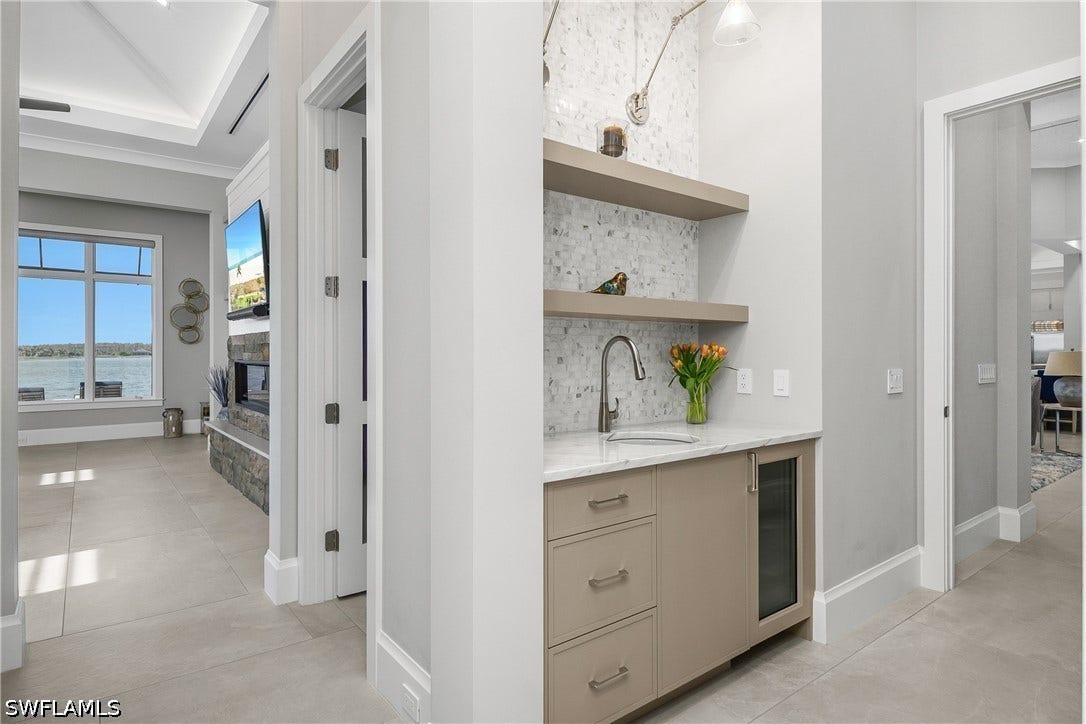 Primary suite entry featuresa morning coffee/beverage bar with sink, beverage cooler, custom sconces and built-in shelving.