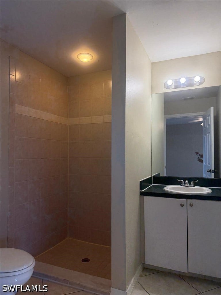4822/4824 Leonard Boulevard S, Lehigh Acres, FL 33973 Tiled shower stall with a built-in shelf, single vanity with a dark countertop, integrated sink, and overhead illumination