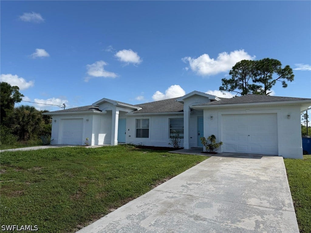 4822/4824 Leonard Boulevard S, Lehigh Acres, FL 33973 Contemporary architecture with a light exterior finish, featuring two single-car garages, a concrete driveway, and a covered entry