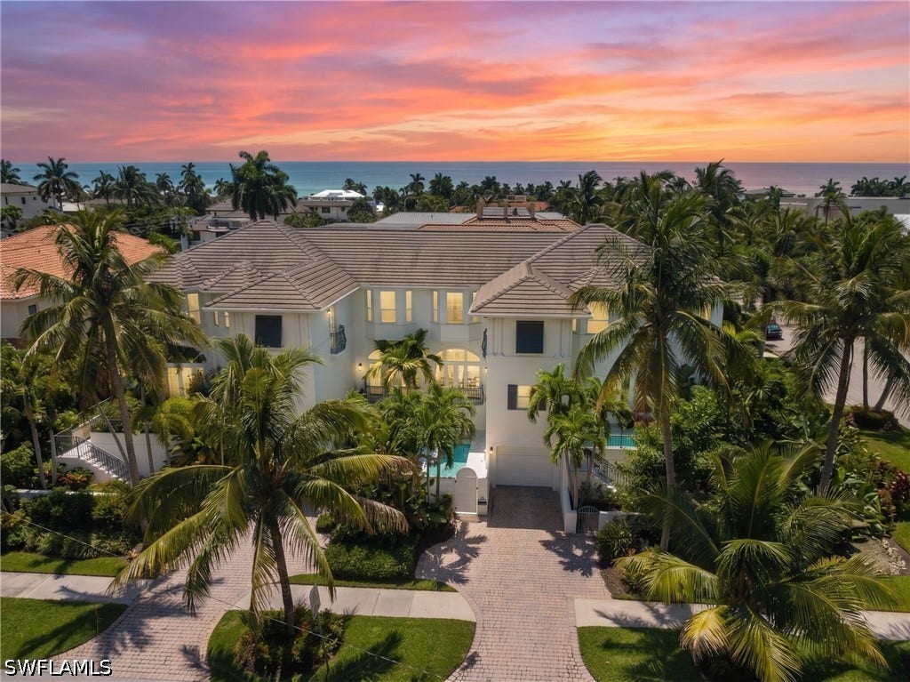 510 2nd Street S, #102, Naples, FL 34102 White stucco exterior with multiple windows, paver driveway, lush landscaping, and tile roof