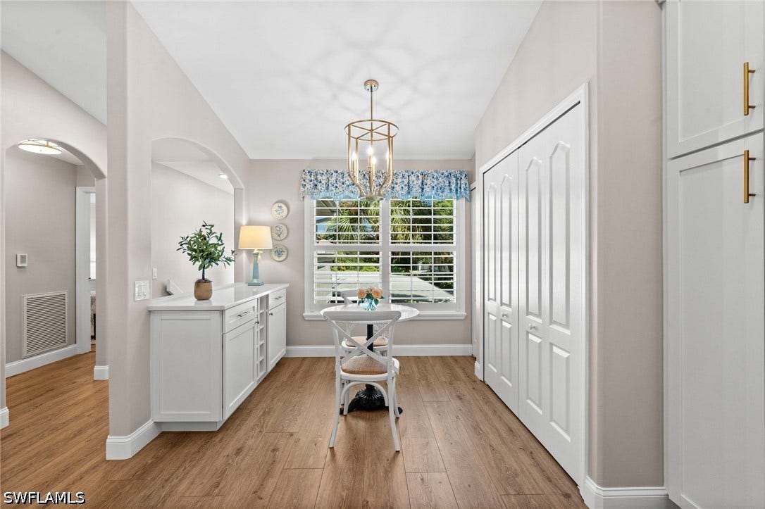Wood-finish flooring, white built-in cabinetry, arched wall opening, shuttered window, and a decorative chandelier