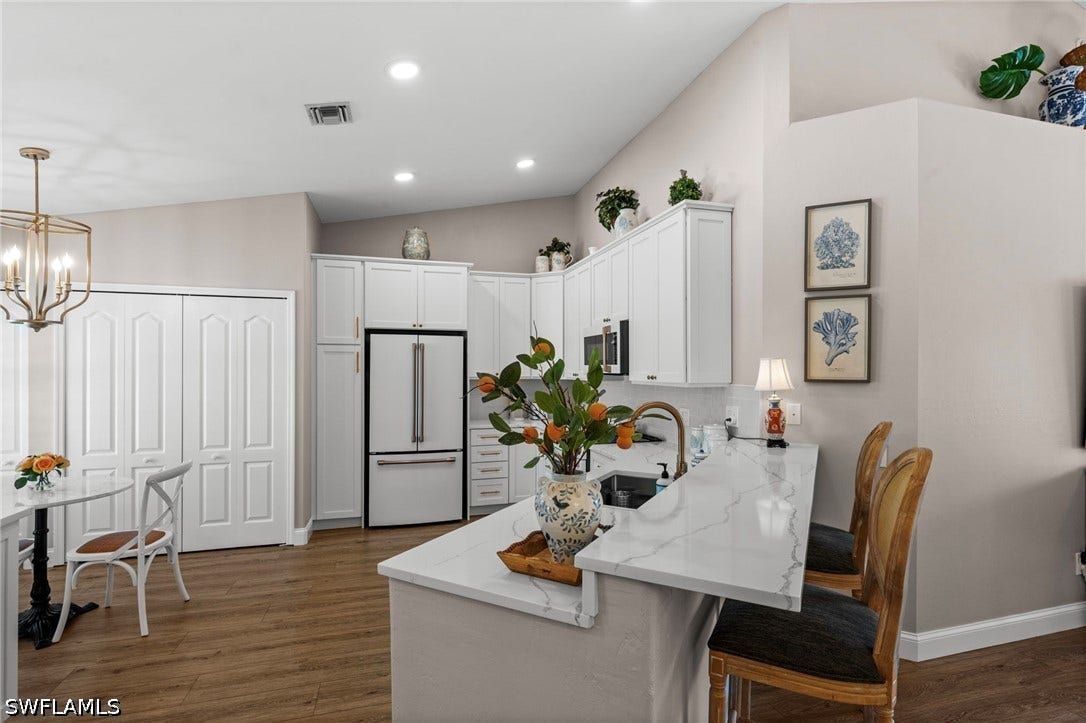 Vaulted ceilings, wood-finish flooring, white cabinetry, integrated stainless steel appliances, and a kitchen island with a waterfall countertop