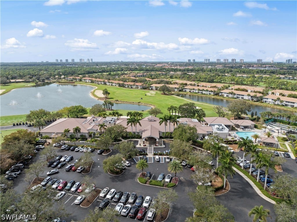 Expansive golf course with multiple water features, clubhouse with covered entry, large outdoor pool, and surrounding residential buildings