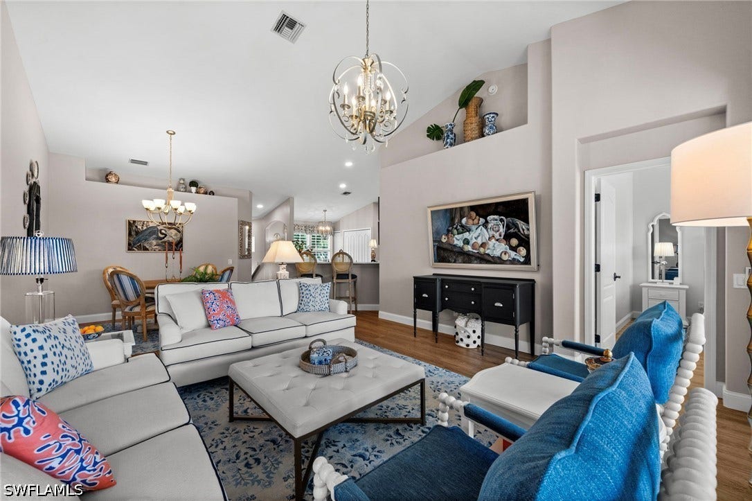 Vaulted ceilings with architectural ledges, gold-finish chandelier, recessed wall niche, wood-finish flooring, and open floor plan
