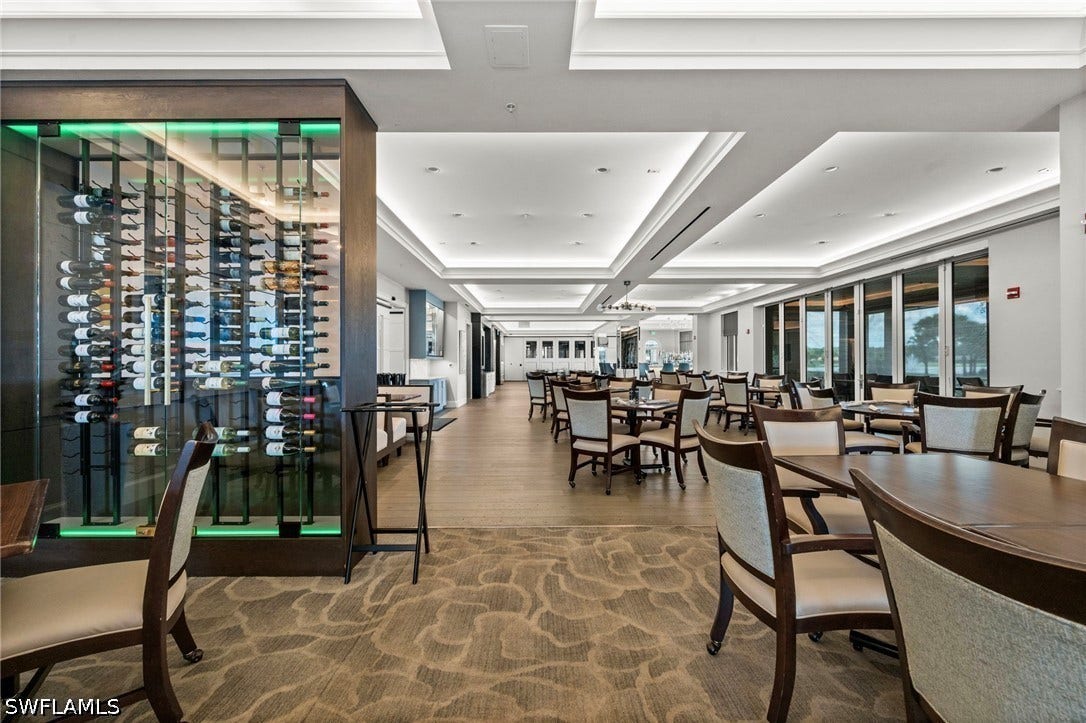 Integrated glass-front wine display with custom lighting, coffered ceiling, recessed lighting, wood-finish flooring, and expansive window wall