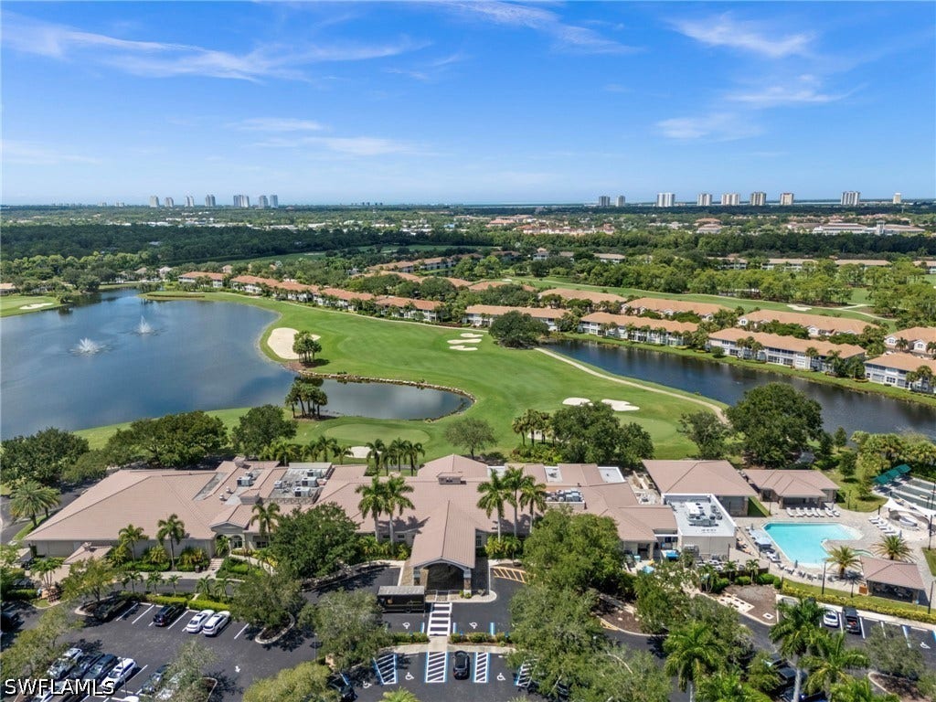 Expansive property featuring a golf course, multiple lakes with water features, a large building complex with a prominent entrance, a swimming pool with surrounding lounge areas, and a paved parking area