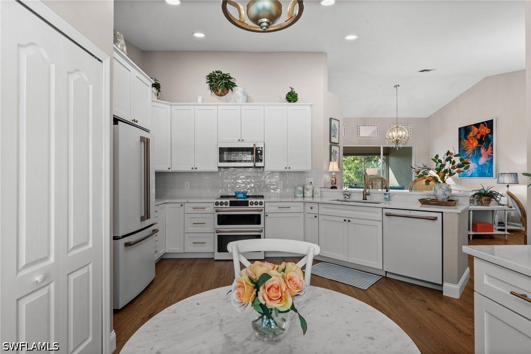 Kitchen featuring white cabinetry, stainless steel appliances, wood-finish flooring, and a subway tile backsplash