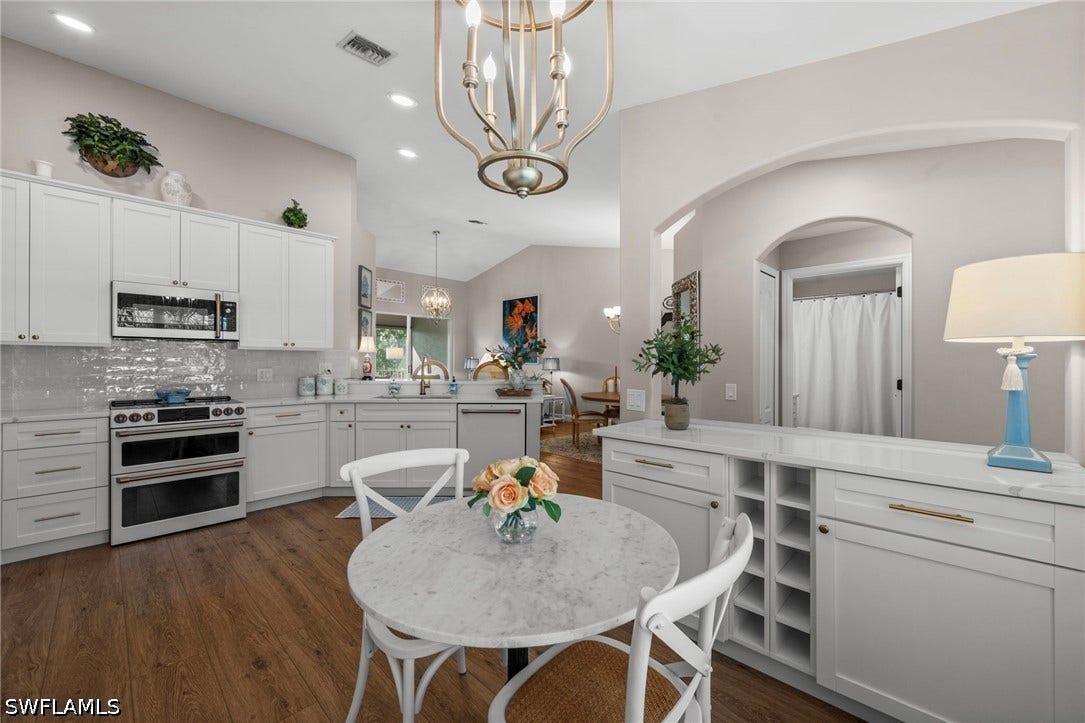 Vaulted ceilings, wood-finish flooring, white cabinetry, integrated stainless steel appliances, and a built-in wine rack