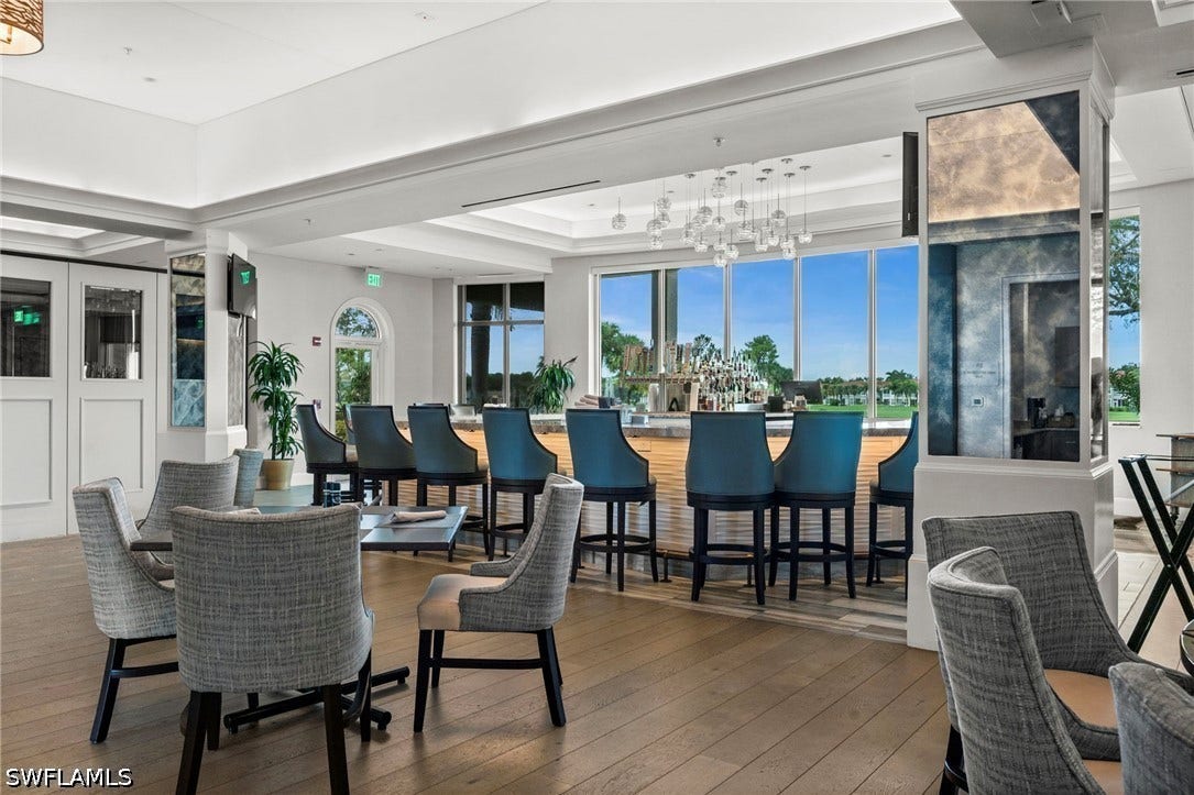 Spacious interior featuring a full-service bar with bar seating, expansive windows, wood-finish flooring, and contemporary pendant lighting