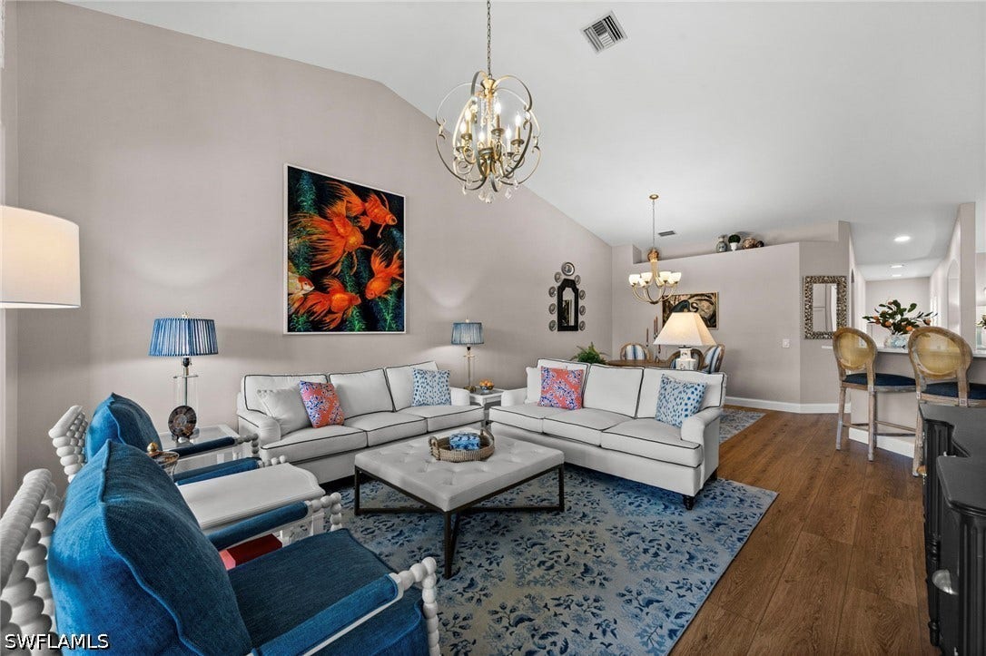 Vaulted ceiling great room with wood-finish flooring, a tiered chandelier, and a breakfast bar with seating