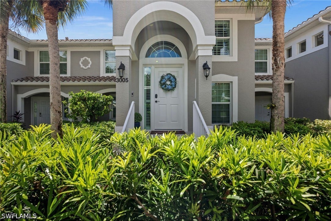 Stucco exterior with arched entryway, white door with sidelights, decorative window trim, and exterior lighting fixtures