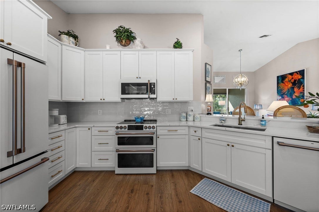 White shaker cabinetry with gold-toned hardware, wood-finish flooring, white subway tile backsplash, and stainless steel appliances