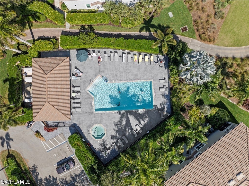 Community swimming pool with an integrated spa, expansive paver deck, adjacent clubhouse, and surrounding tropical landscaping
