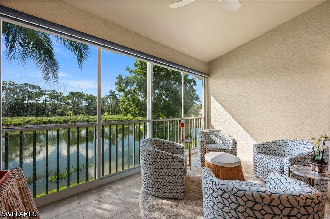 Screened balcony with tiled flooring, textured ceiling, ceiling fan, and expansive water feature with surrounding trees
