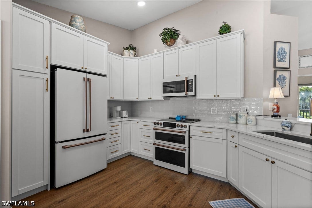 Kitchen featuring white shaker-style cabinetry, a built-in double oven, wood-finish flooring, a stainless steel sink, and light-toned countertops