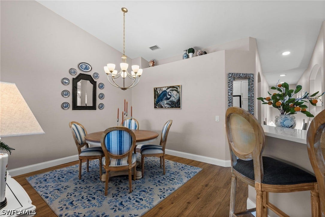 Vaulted ceiling, wood-finish flooring, and an elegant chandelier illuminate the dining area