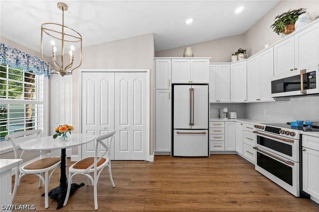 Vaulted ceilings, wood-finish flooring, white cabinetry, integrated stainless steel appliances, and a built-in pantry