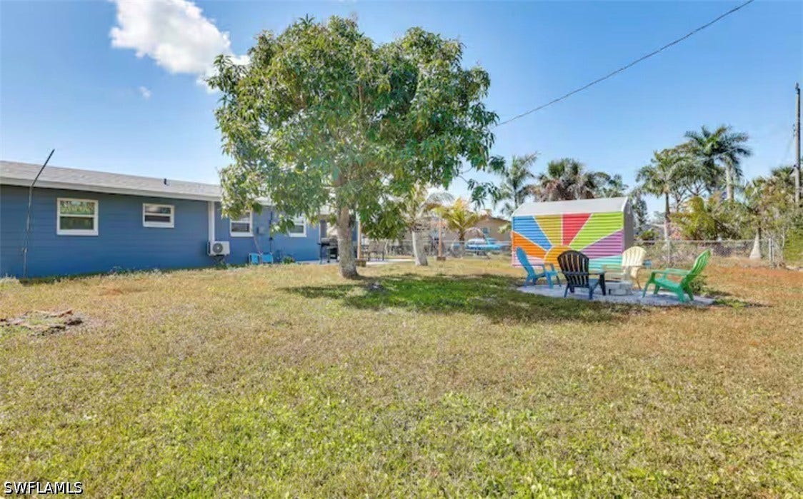 4630 New Haven Drive, Fort Myers, FL 33908 Expansive grass backyard with mature tree, blue exterior siding, white window frames, and a colorful storage shed