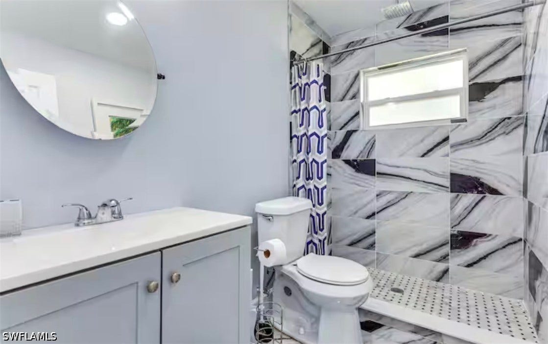 4630 New Haven Drive, Fort Myers, FL 33908 Vanity with light-colored countertop, wall-mounted circular mirror, chrome faucet, and tiled shower with a window