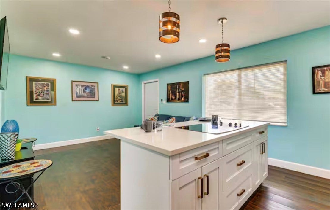 4630 New Haven Drive, Fort Myers, FL 33908 Kitchen island with a light-toned countertop, integrated cooktop, white cabinetry, and brass hardware