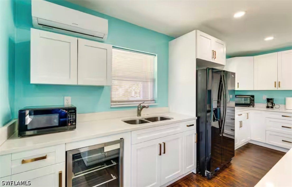 4630 New Haven Drive, Fort Myers, FL 33908 White shaker-style cabinetry with gold-tone hardware, a dual-basin sink with a gooseneck faucet, a built-in beverage cooler, and wood-finish flooring