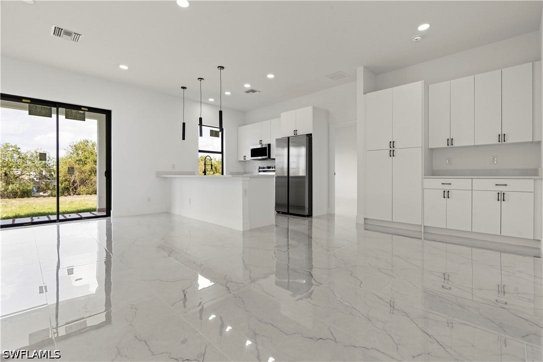 532 Lone Star Lane, Lehigh Acres, FL 33974 White kitchen cabinetry with black hardware, stainless steel appliances, and a kitchen island with pendant lighting